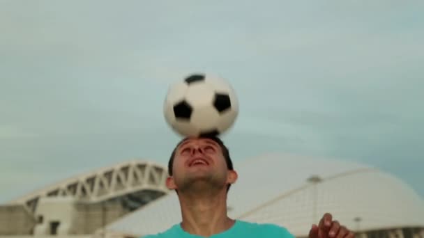 Ein Mann mit einem Fußballball mit einem Ball vor dem Hintergrund des Stadions. — Stockvideo