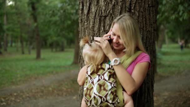 Una donna con un bambino in fionda parla su uno smartphone — Video Stock