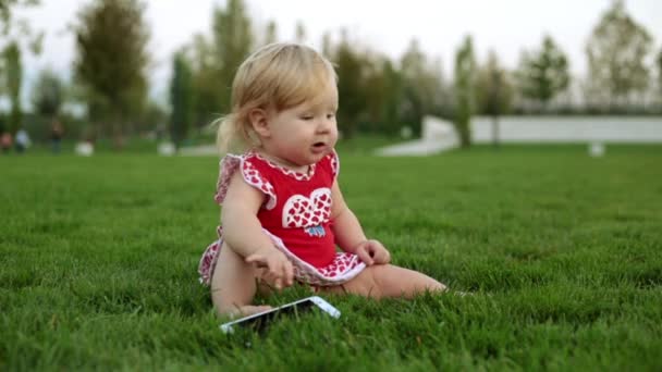 Kindje met smartphone op het gras in het park — Stockvideo