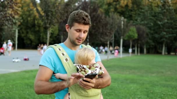 Muž s dítětem v šátku používá smartphone. — Stock video