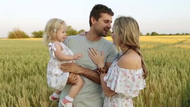 Glückliche junge Familie mit Kind im Hintergrund eines Weizenfeldes. — Stockvideo