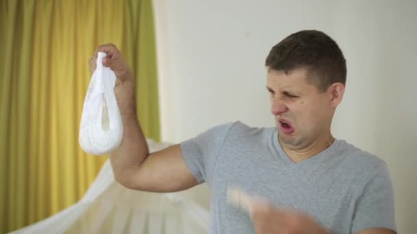 Un hombre con un alfiler de ropa en la nariz sostiene un pañal de bebé . — Vídeos de Stock