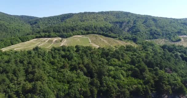 Aéreo - Colinas verdes, floresta e árvores, estrada de terra . — Vídeo de Stock