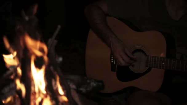 Um homem toca guitarra à noite junto ao fogo. . — Vídeo de Stock