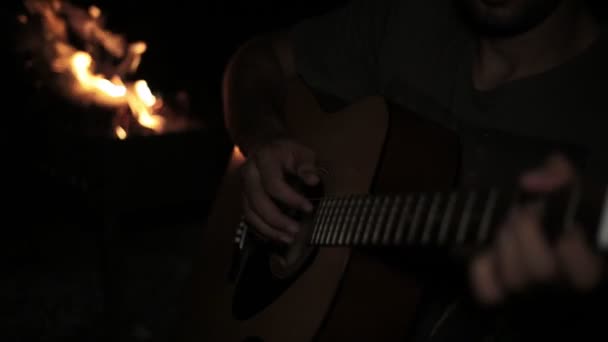 En man spelar en gitarr i en mörk mot bakgrund av en brand. — Stockvideo