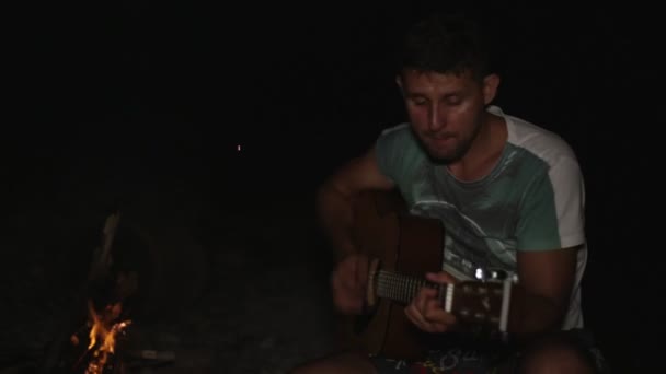 Ein Lagerfeuer und ein Mann, der Gitarre spielt. — Stockvideo
