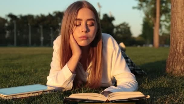 Ένα νεαρό κορίτσι βρίσκεται στο γρασίδι και να διαβάζει ένα βιβλίο. — Αρχείο Βίντεο