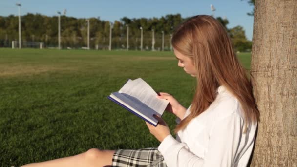 Una joven está leyendo un libro en el parque. . — Vídeos de Stock