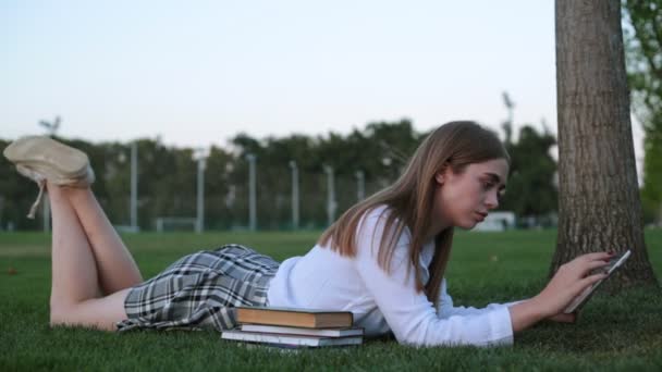 Um estudante em um parque com livros e um tablet . — Vídeo de Stock