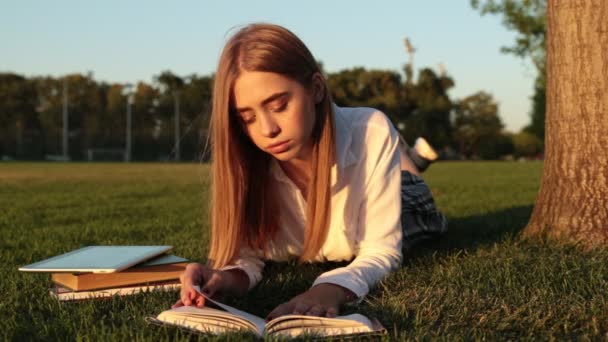 Hermosa chica está leyendo un libro en el parque . — Vídeo de stock