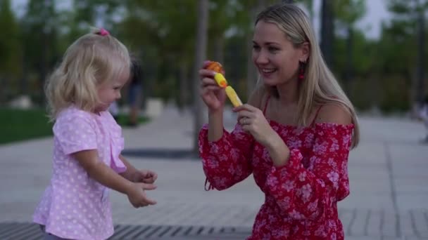 Kvinna och barn som blåser såpbubblor i parken. — Stockvideo