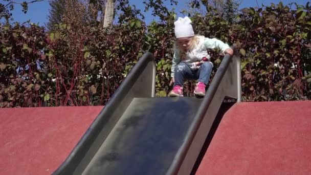Una ragazza scivola giù da uno scivolo in un parco giochi per bambini. Il bambino rotola giù per una collina . — Video Stock