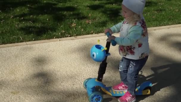 En tjej rider en skoter i parken. barn rider en barnens skoter. — Stockvideo