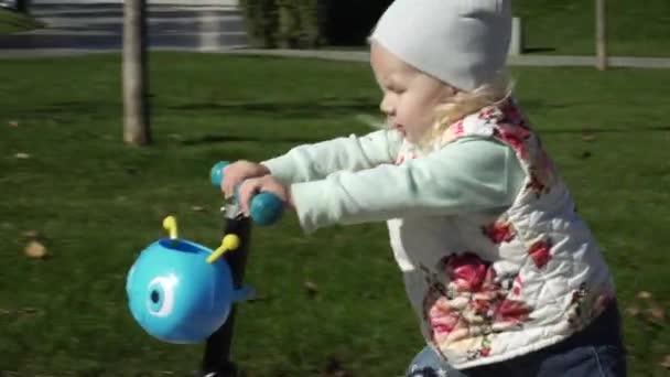 Весела дитина катається на скутері в парку . — стокове відео