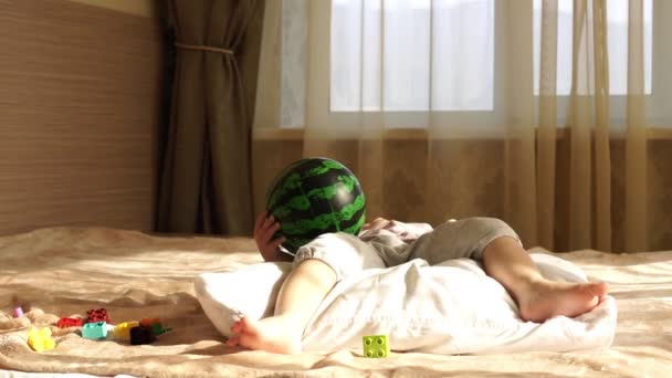 Маленька дівчинка блондинка грає вдома на ліжку з м'ячем . — стокове відео