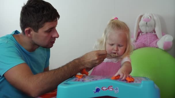 A man feeds his daughter porridge. A father feeds a small child. — Stock Video