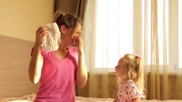 Eine Frau hält angewidert eine schmutzige Windel in der Hand. Kind und Mutter im Zimmer. — Stockvideo