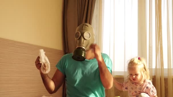 Een jonge vader in een gasmasker verandert een vuile baby luier. — Stockvideo