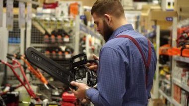 Bir adam bir donanım mağazasında bir chainsaw seçer.