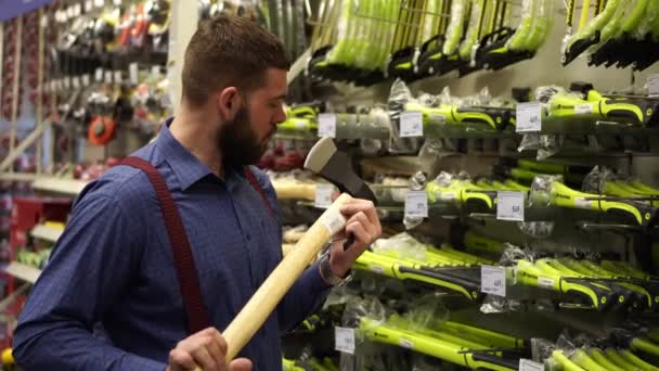Um homem numa loja de ferragens escolhe um machado . — Vídeo de Stock