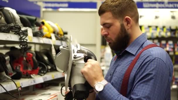 Ένας άντρας σε ένα κατάστημα υλικού επιλέγει ένα εργαλείο δύναμης. — Αρχείο Βίντεο