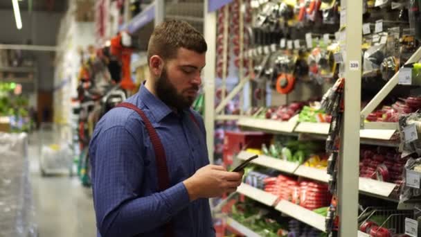 En man med en smartphone i en järnaffär. — Stockvideo