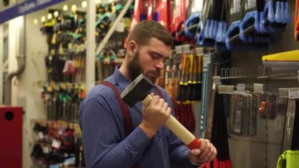 Um homem numa loja de ferragens escolhe uma marreta. . — Vídeo de Stock