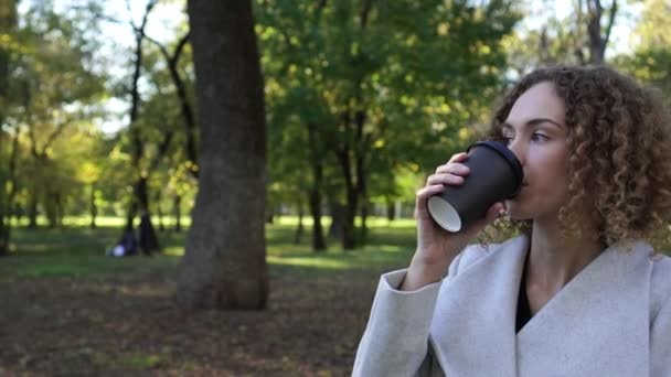 Vacker ung kvinna dricker kaffe i parken våren. — Stockvideo