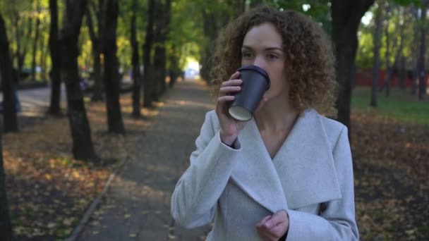 Genç iş kadını sonbahar parkta kahve içiyor. — Stok video