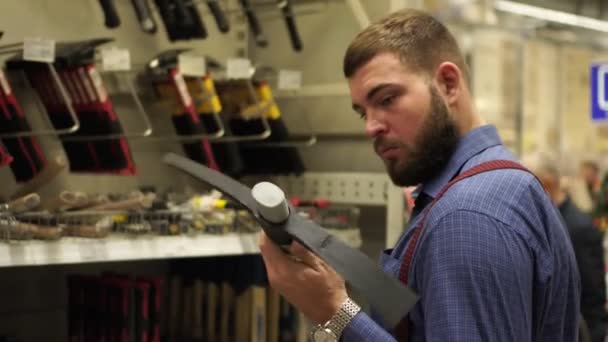 Un hombre con barba elige una herramienta de mano en una ferretería . — Vídeos de Stock