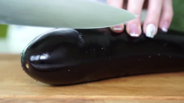 Une femme coupe une aubergine avec un couteau dans la cuisine, gros plan . — Video