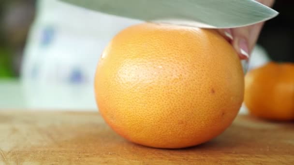 Eine Frau schneidet in der Küche mit einem Messer eine Grapefruit. — Stockvideo