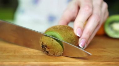 Kadın mutfakta, ağır çekim kivi keser.