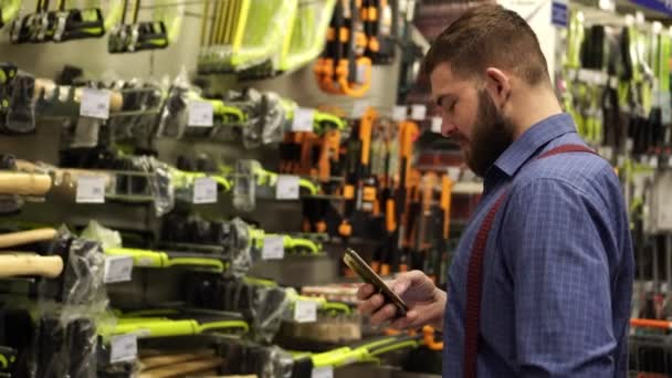 En man i en järnaffär använder en smartphone. — Stockvideo