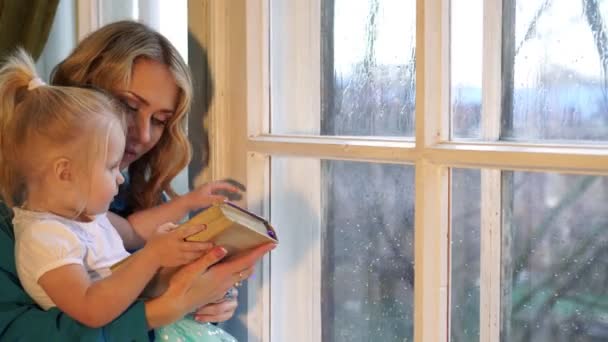 Glückliche Familie Mutter Kind Tochter kleines Mädchen liest ein Buch am Fenster — Stockvideo