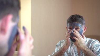 Genç bir adam kozmetik bir maske yüz için kullanır..