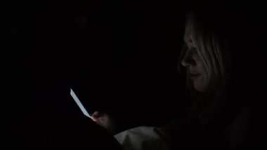 Bir kadın bir yatakta bir akıllı telefon ile karanlıkta.