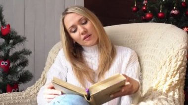 Genç kadın bir Noel ağacı arka plan üzerine bir kitap okuma.