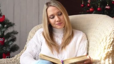 Kadın sandalyede bir Noel ağacı arka plan üzerine bir kitap okuma.