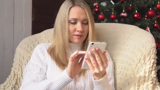 Mulher com um smartphone na árvore de Natal . — Vídeo de Stock