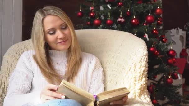 Mulher bonita lendo um livro no fundo da árvore de Natal . — Vídeo de Stock