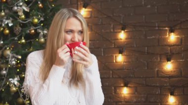 Bir Noel ağacı arka plan üzerinde kahve veya çay içme bir rahat kazaklı genç bir kadın.