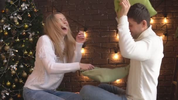 Casal jovem lutando com travesseiros no fundo da árvore de Natal . — Vídeo de Stock