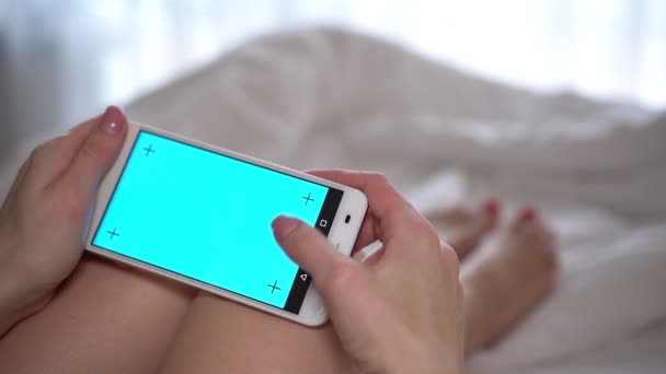 Egy nő használ egy smartphone az ágyon egy üres, kék képernyő. — Stock videók
