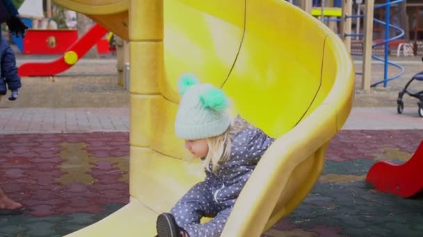Un niño pequeño montando un tobogán en el patio de recreo . — Vídeos de Stock