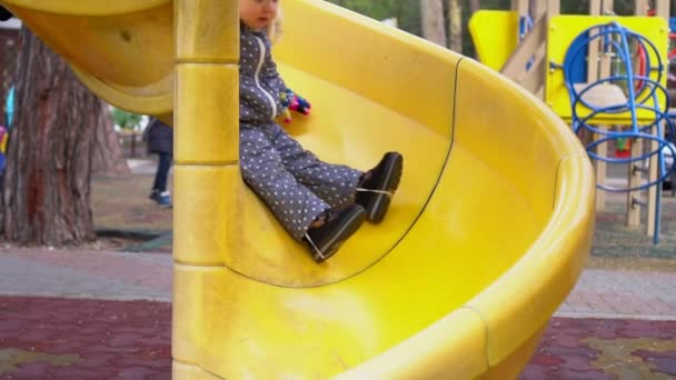 A small child rides in the winter with slides on the playground, slow motion. — Stock Video