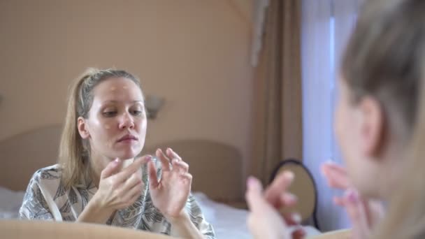 Een vrouw thuis zet een komeet masker op haar gezicht. Gezichtsbehandeling huidverzorging. — Stockvideo