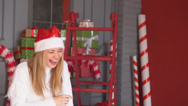 Natale, una giovane donna con un cappello da Babbo Natale ride emotivamente . — Video Stock