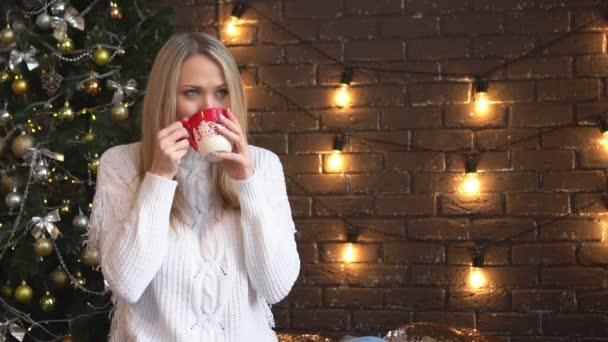 Natale, una bella donna con un maglione bianco che beve da una tazza . — Video Stock