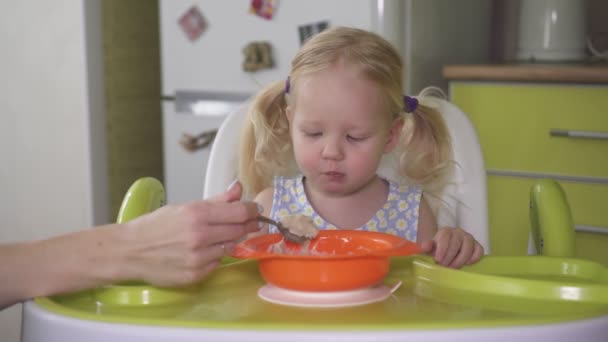 Mom feeds her little daughter porridge with a spoon. — Stock Video